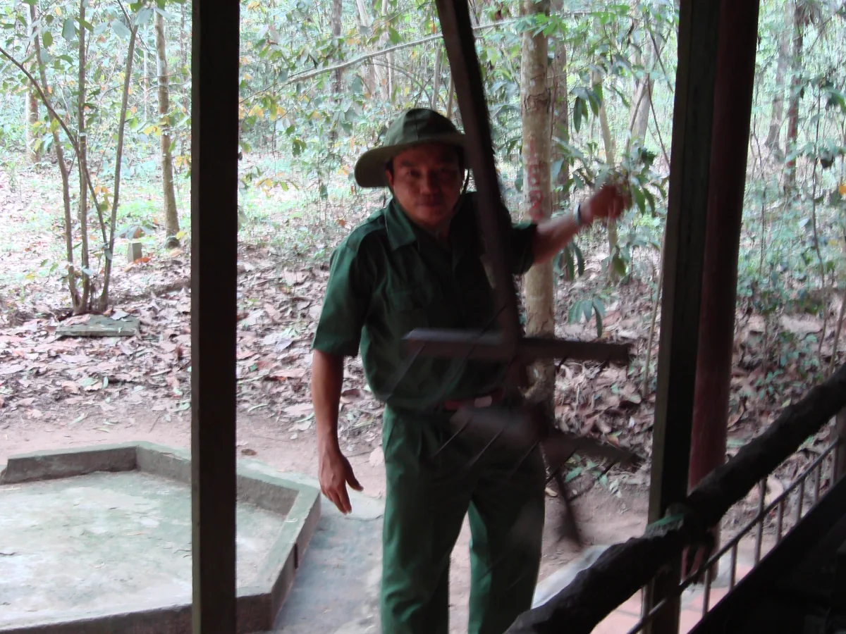 A person demonstrating a camouflaged Cu Chi trap door in the jungle floor